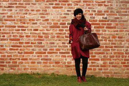 Young freckled caucasian brunette girl in purple overcoat and black beret posing in front of brick wall and smiling.の写真素材