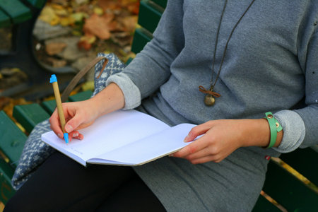 Girl in grey dress siting on the green bench writing notes into her notepad. Writer concept photo.の写真素材