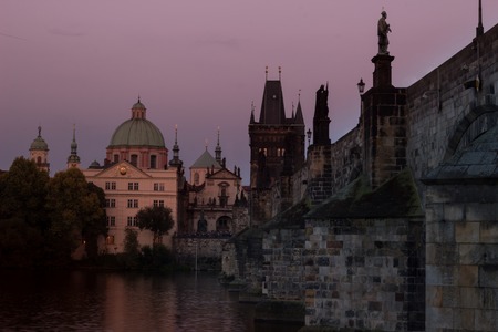 Violet moody picture of the Charles Bridge and bankside of the Vltava river with the Church of Francis of Assisi. Beautiful evening picture of Prague typical sightseeing.の写真素材