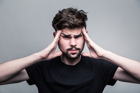 Young man feeling pain, frowning with hand on head with gray backgroundの写真素材