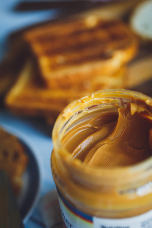 Open jar of peanut butter and toasts on background