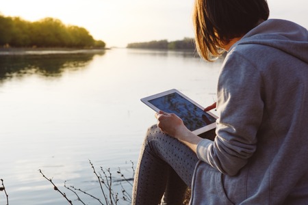 Young girl works with the tablet on the banks of the riverの写真素材