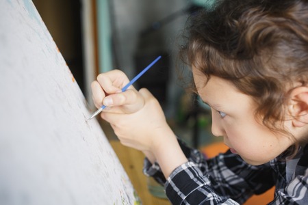 eight year old girl in a plaid shirt with enthusiasm that paints with a brush on canvasの写真素材