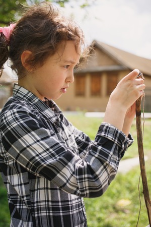 girl in a plaid shirt plays one on the street with a rope and a wooden stick in the village during summerの写真素材