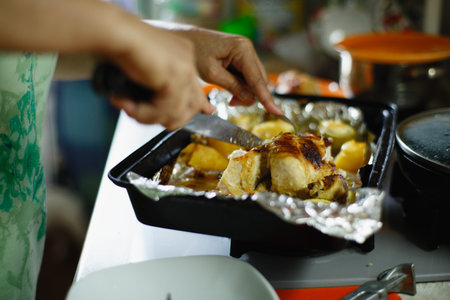 a woman cut in the kitchen juicy fried chicken on the baking sheet with vegetables for dinnerの写真素材