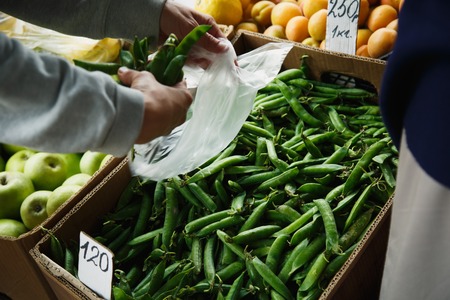 woman with your hands puts the pods of young peas in a plastic bag from a large box on the marketの写真素材