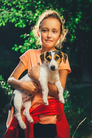 girl holding a small dog breed Jack Russell Terrier smiles and looks at the camera on a summer dayの写真素材