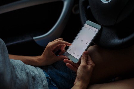 woman looking something in the phone sitting in the car on a summer dayの写真素材