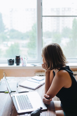 Young woman sitting at a Desk with a computer and looking out the windowの写真素材