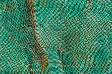 Deformed rusty metal surface is covered with green metal mesh . Background