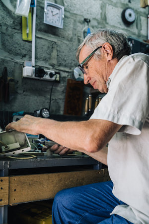 Side view of elderly man in glasses working at table in garage