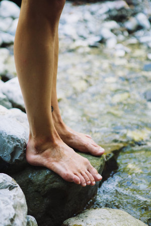 Close-up of unrecognizable barefoot woman standing on wet stone at river