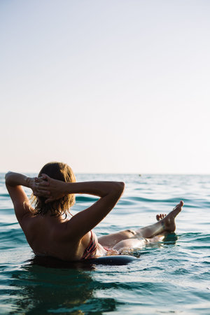 Rear view of unrecognizable young woman with short hair in bikini swimming on air ring with widened...