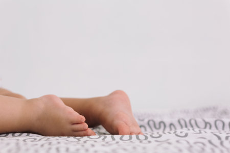 Close-up of unrecognizable baby lying barefoot on patterned bedsheet