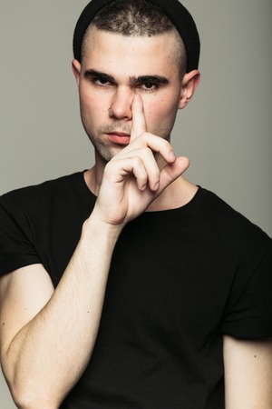 Man in black t-shirt against grey background putting finger to his faceの写真素材