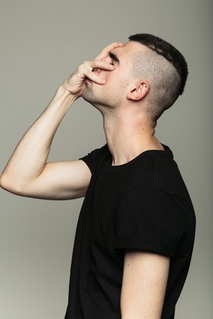 Side-view of man with shaven temples in black t-shirt, who feeling shame and holding his right hand on face. Isolatedの写真素材