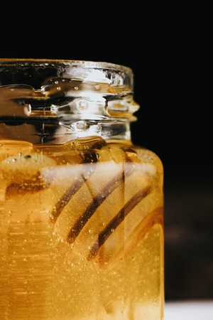 Macro crop view of glass honey jar with honey stick inside appearing slowly.の写真素材