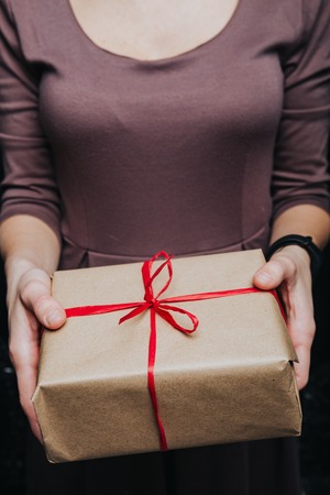 Close up crop hands holding wrapped present with red ribbon isolated on black.の写真素材