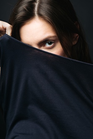 Young woman looking at camera and covering her face with her black cloth. Vertical studio shotの写真素材