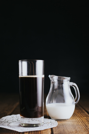Jar of milk and glass of coffee against dark backgroundの写真素材