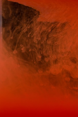 Red paint on the dark background doing stains because of drop into water. Looks like blood.の写真素材