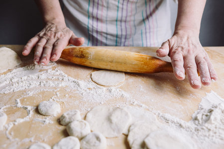 Image of two womans hands making meat dumpling with wooden rolling pin.