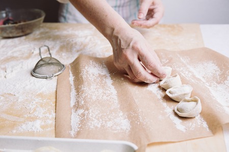 Close up view of woman folds the raw dumplings on a sheet of parchmentの写真素材