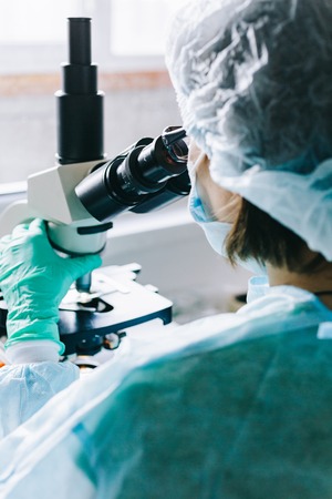 Scientist in blue medical gloves and uniform learning samples with microscope in laboratory.の写真素材
