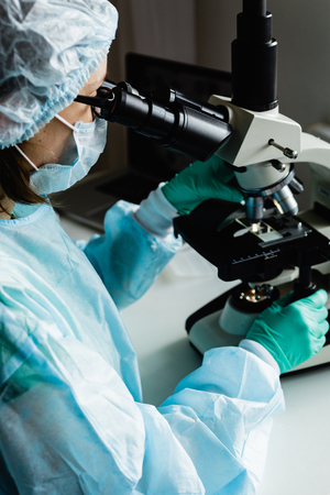Scientist in blue medical gloves and uniform learning samples with microscope in laboratory.の写真素材