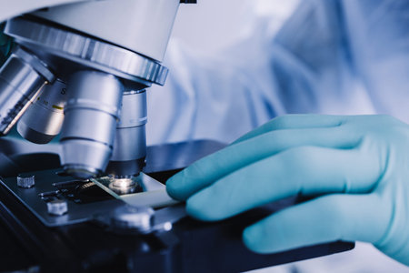 Close up view of scientist hands with gloves set the sample in the microscope for research