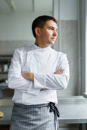 Young male chef posing with hands crossed at kitchen.の写真素材