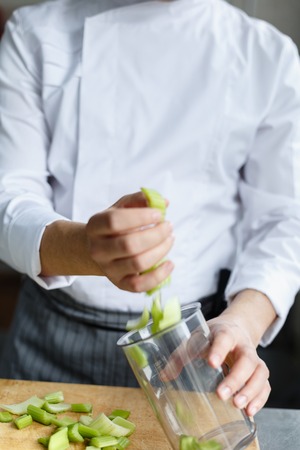 Crop hands of male chef putting cut celery in content for preparing fresh smoothie.の写真素材