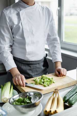 Crop faceless shot of male im uniform cutting celery on cutting board for preparing smoothie.の写真素材