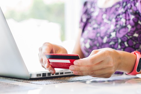 Anonymous woman pays for credit card purchases through the Internet sitting in indoor cafe with laptop.の写真素材