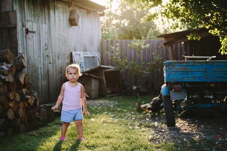 Little boy standing near pile of logs and playing in yard of farmhouse.の写真素材