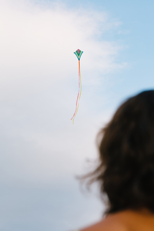 Crop back view of girl standing and looking at kite flying high in sky.の写真素材