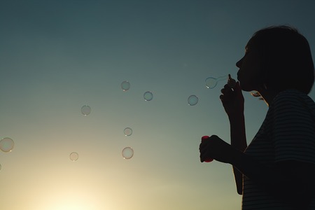 Girl inflates soap bubbles at sunset. Rear view.の写真素材