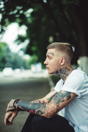 Young casual man with tattoos all over body in casual t-shirt posing at street looking away.の写真素材