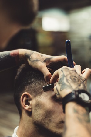 Crop stylish applying foam on customers cheeks for shaving while working in barbershop.の写真素材