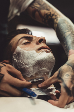 Crop stylish applying foam on customers cheeks for shaving while working in barbershop.の写真素材