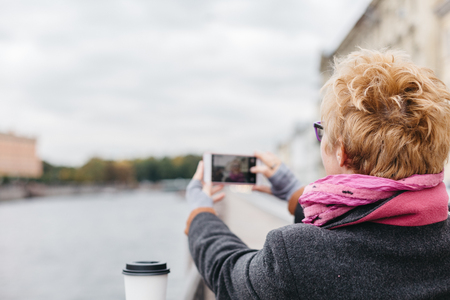Back view of adult blonde woman taking smartphone shots from esplanade.の写真素材