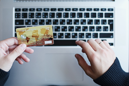 Crop shot from above of woman holding credit card while purchasing online with laptop.の写真素材