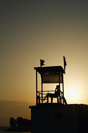 Black silhouette of observation tower and person in it on coastline in sunset time.の写真素材