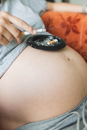 Anonymous pregnant woman smokes a cigarette, put the ashtray on the stomachの写真素材