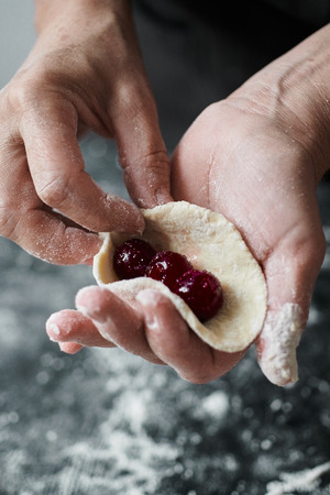 Woman cook manually sculpts dumplings stuffed with cherries with sugarの写真素材