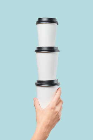 Crop hand holding white paper cups with black lids in stack against blue backgroundの写真素材
