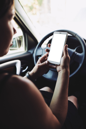 Woman sitting behind the wheel of car looking at the screen of the smartphoneの写真素材