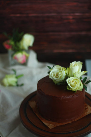 Chocolate cake on wooden background with white rose flowers