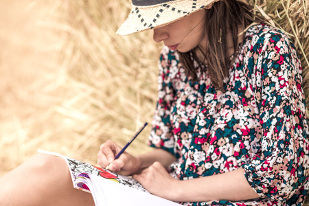 the brunette sitting on the hay and coloring, with different bright pencils and slim legs and hatの写真素材
