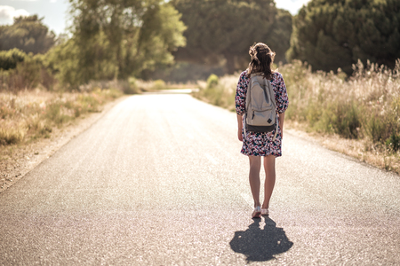 bright dreesed girl with backpack on the way. the empty roadの写真素材